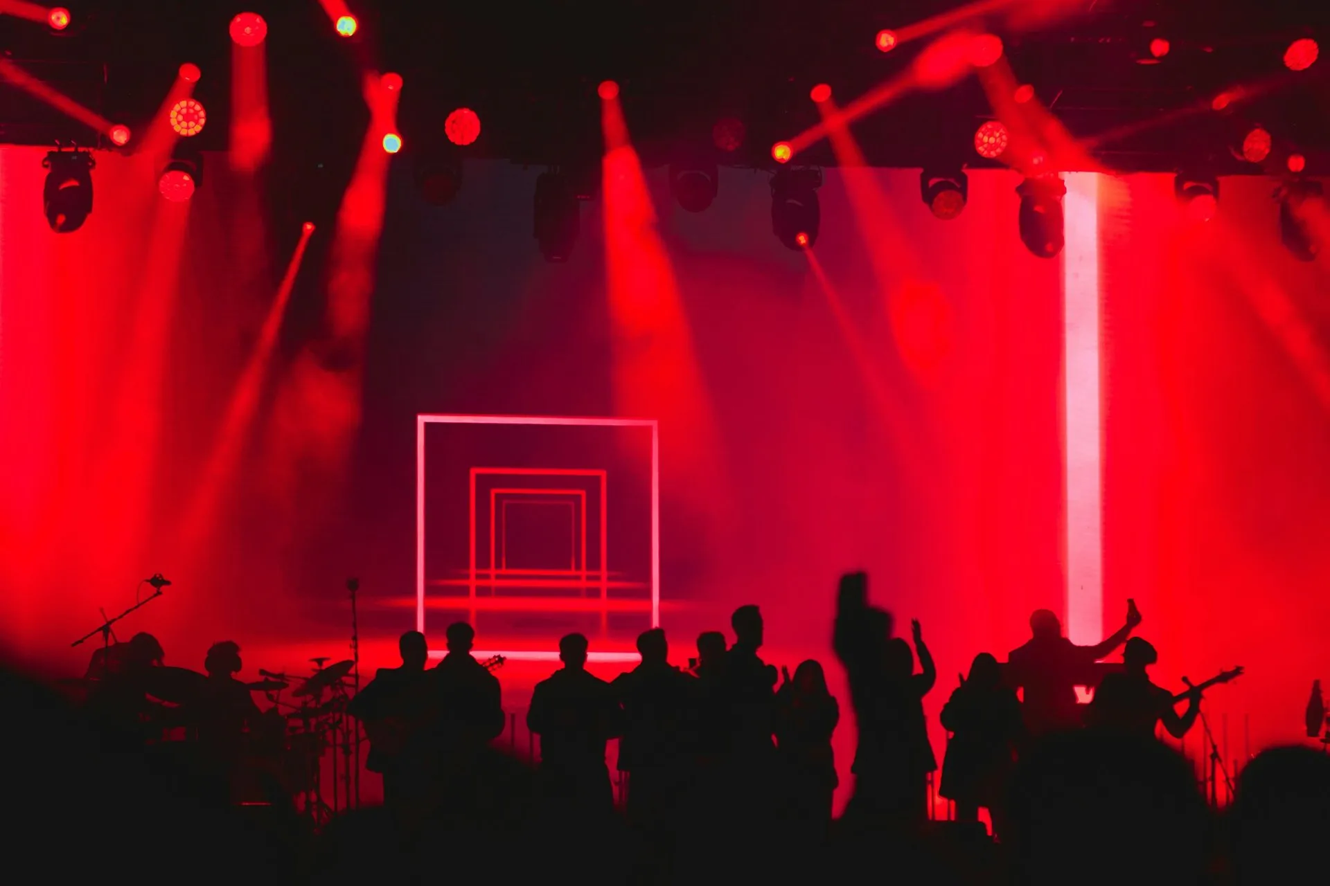 A crowd in silhouette in front of a stage washed in red light