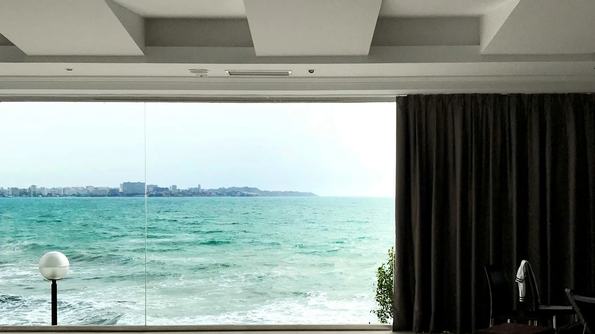 A bright open-plan room with a floor-to-ceiling window looking out over the sea