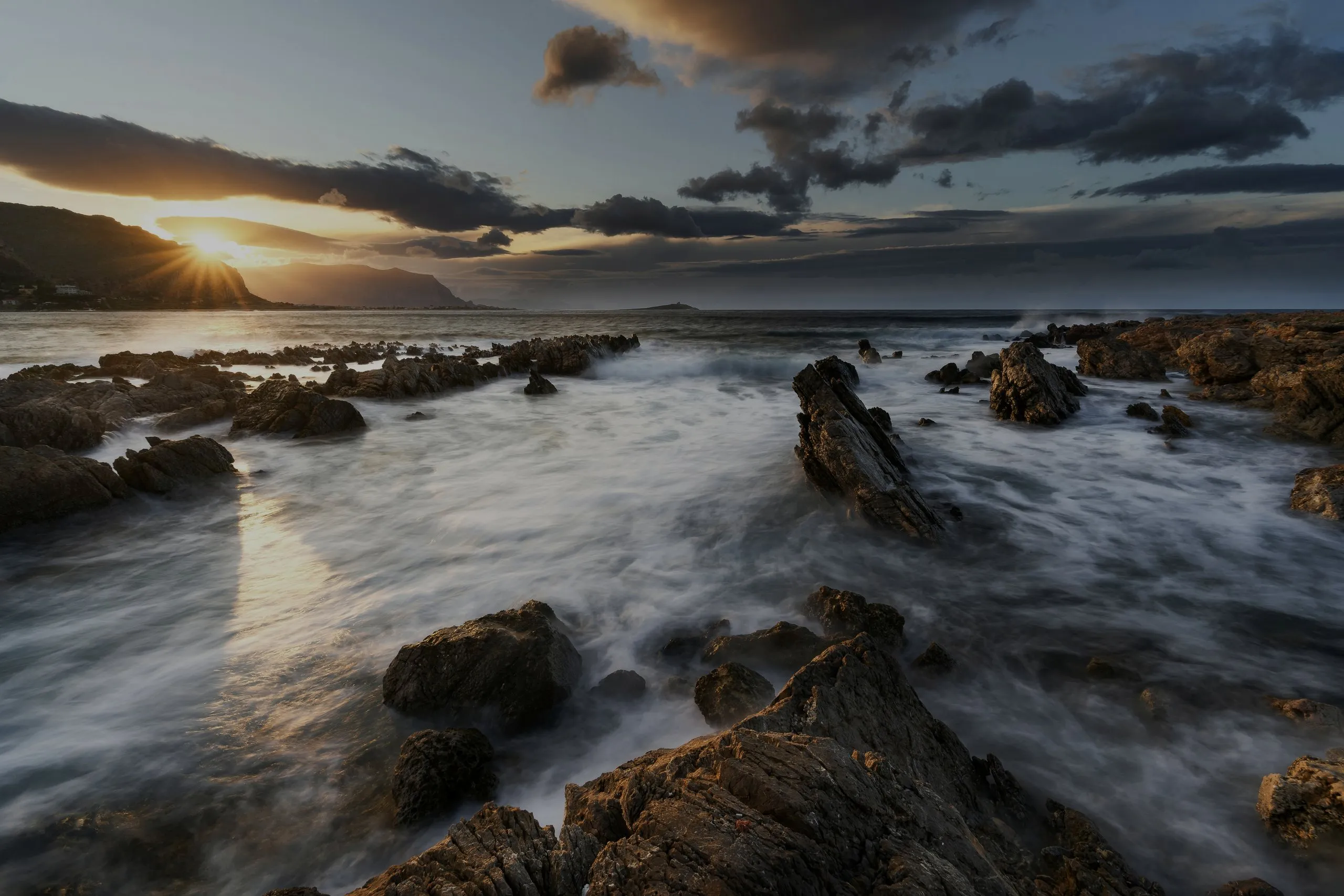 Waves running in over dark rocks on the coast at dusk