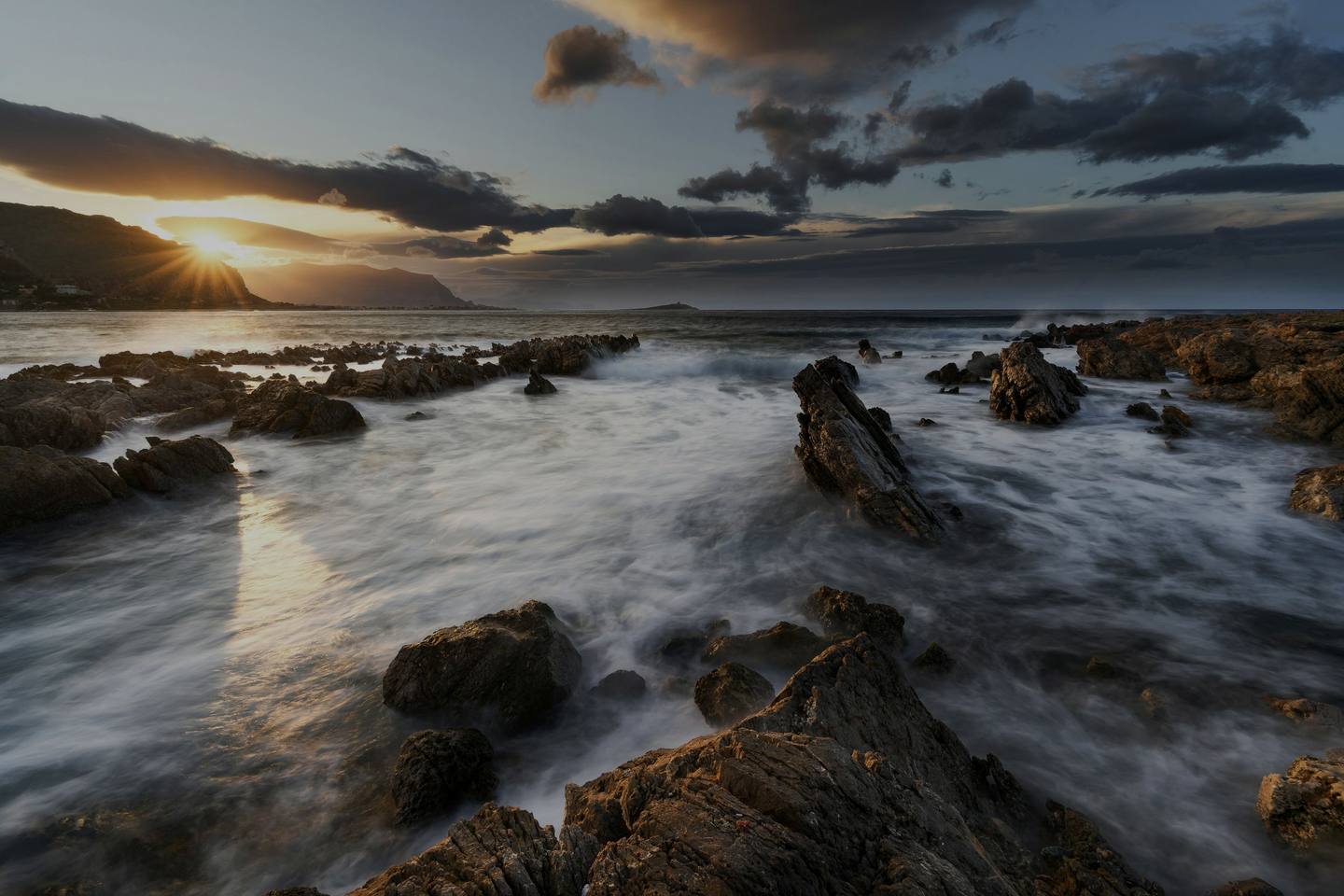 Waves running in over dark rocks on the coast at dusk